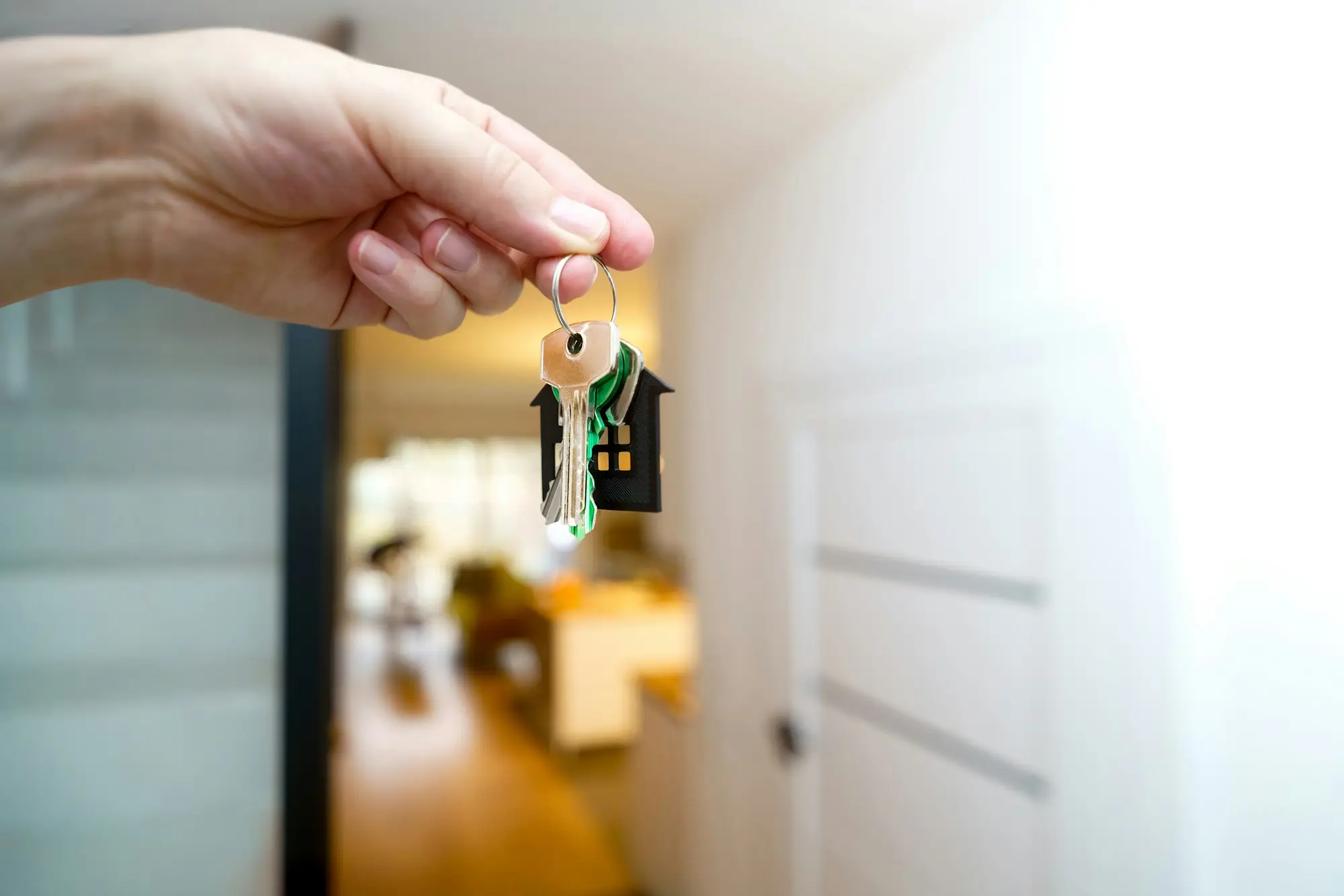 Hand holding house keys in front of a home with a business van parked outside